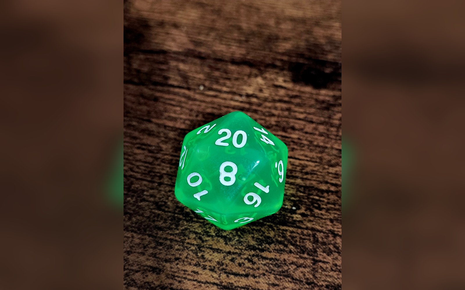 A translucent green twenty-sided die showing the number 20 face up on a wooden surface